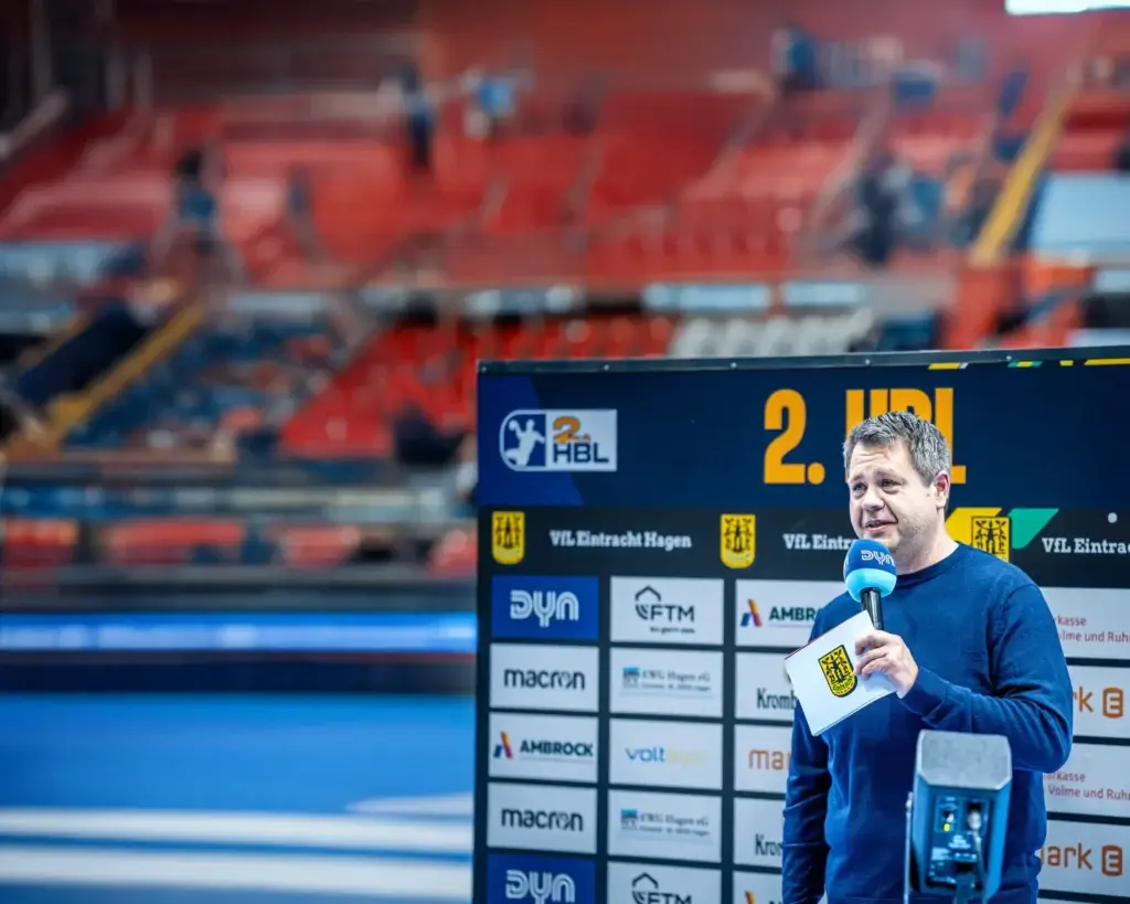 Andreas Klement als Handball Kommentator bei einem Spiel der 2. Handball Bundesliga für Eintracht Hagen mit Mikrofon am Spielfeldrand
